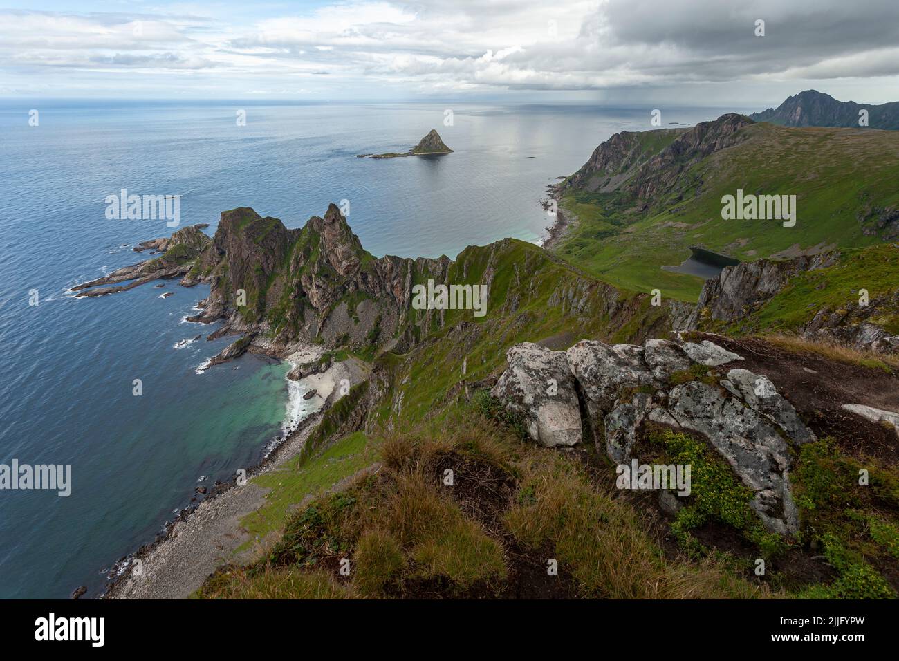 Måtind lookout at a rocky seascape bellow it. View from a mountain top next to the Norway sea with steep cliffs, white sandy beach and a greenery. Stock Photo