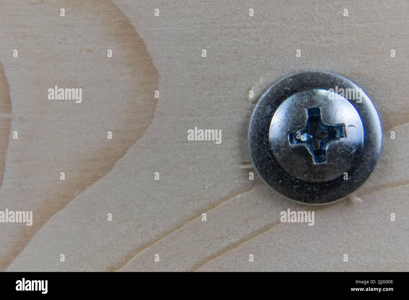 Close-up of the head of a galvanized self-tapping screw with a press washer, screwed into a wooden board. Phillips type slot - PH. Place for text or l Stock Photo