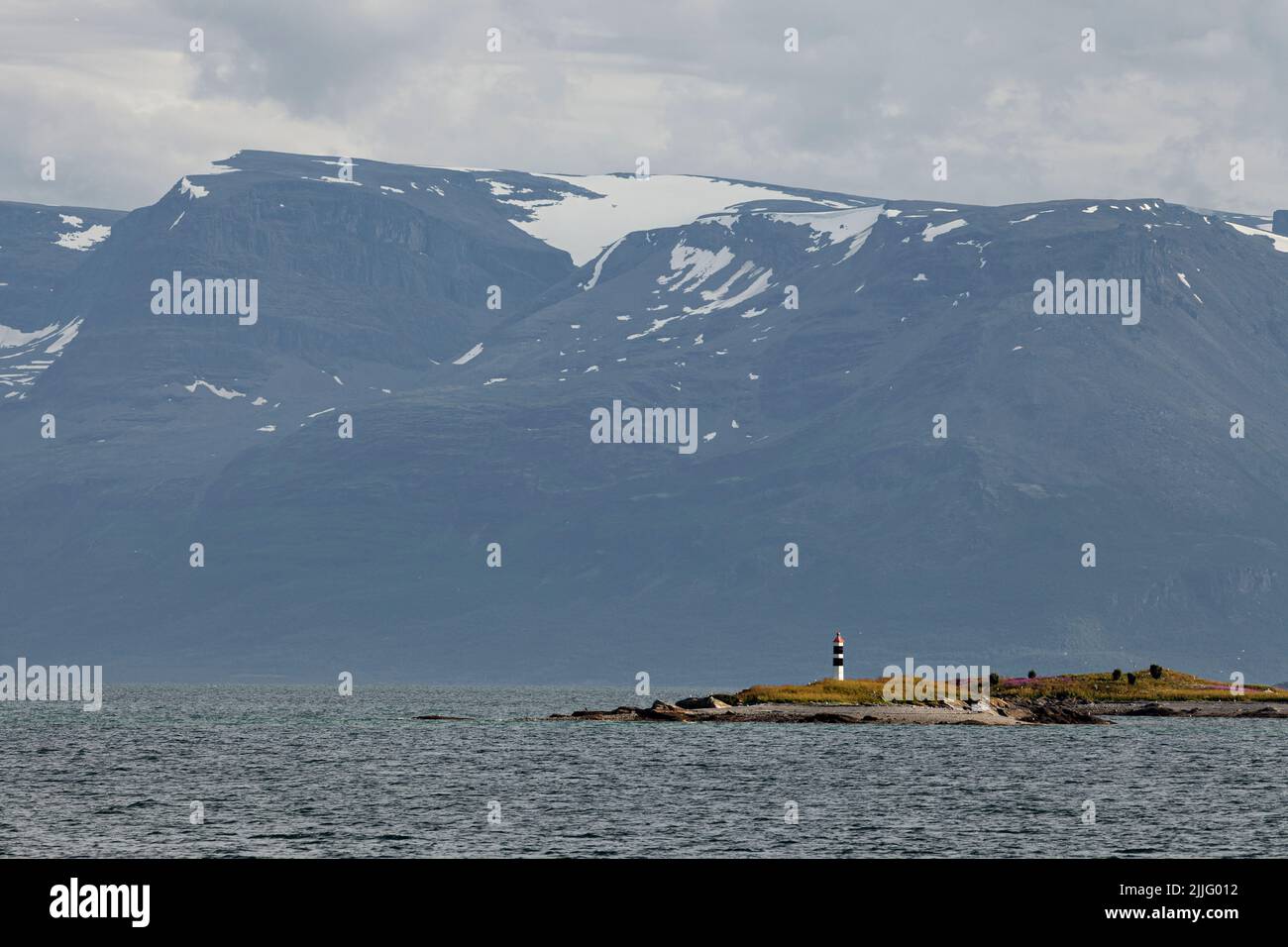 Lighthouse on a small island in Norway with a huge snow covered mountain behind it. Stock Photo