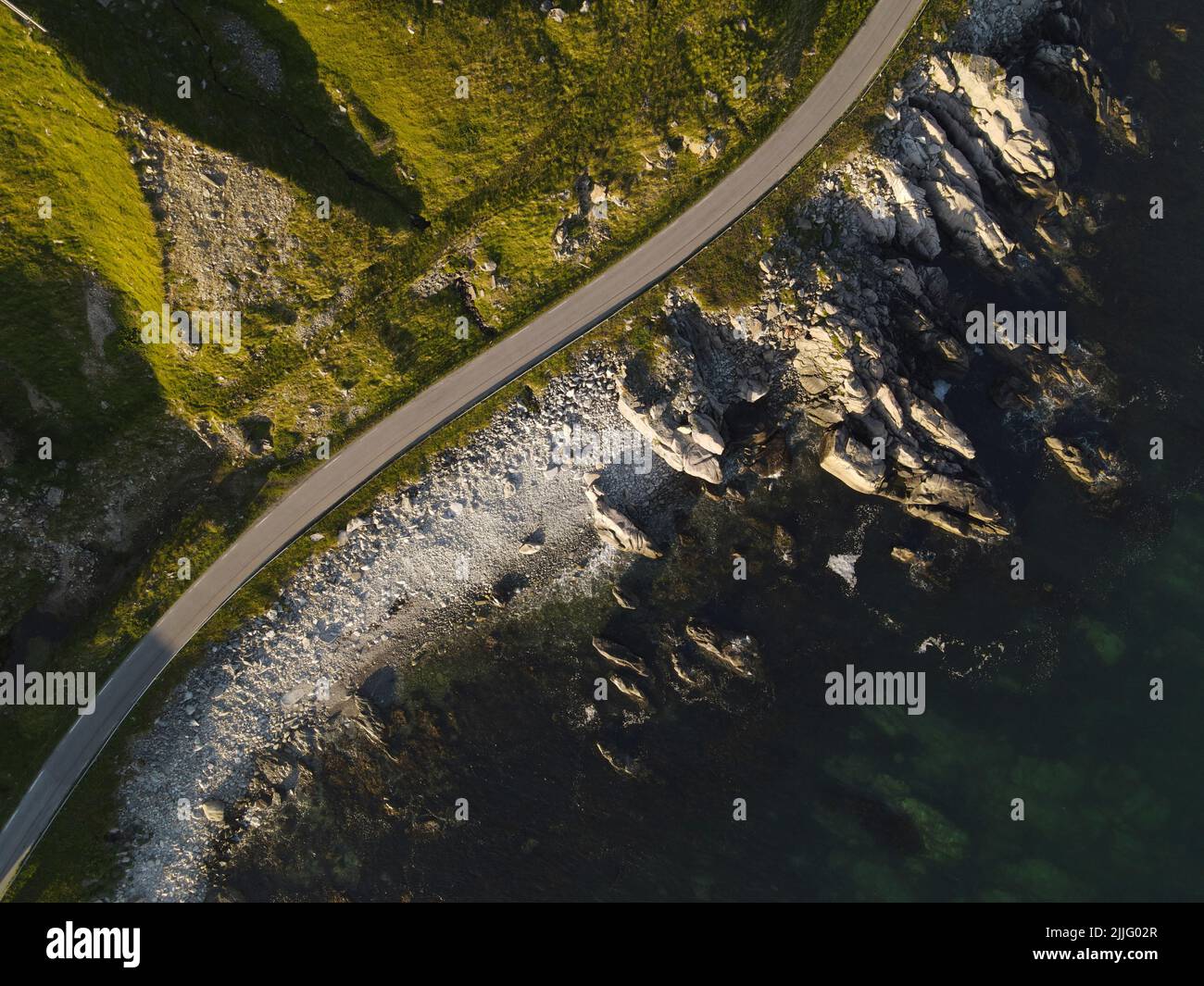 Top down view of a road on a sea shore. Cliffs covered with greenery, rocky shore and a dark blue sea. Stock Photo