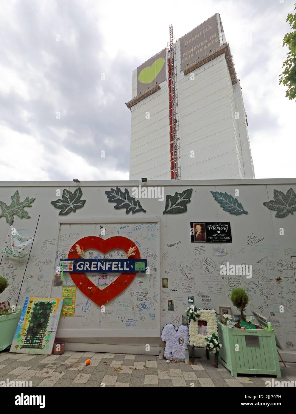 Grenfell Tower fire tragedy block, shown behind the memorial wall for the 72 victims. Grenfell United, Forever, after the cladding fire in 2017 Stock Photo