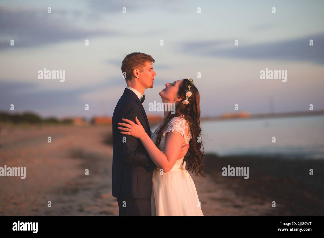 A young romantic bride and groom posing embracing on a beach at sunset Stock Photo