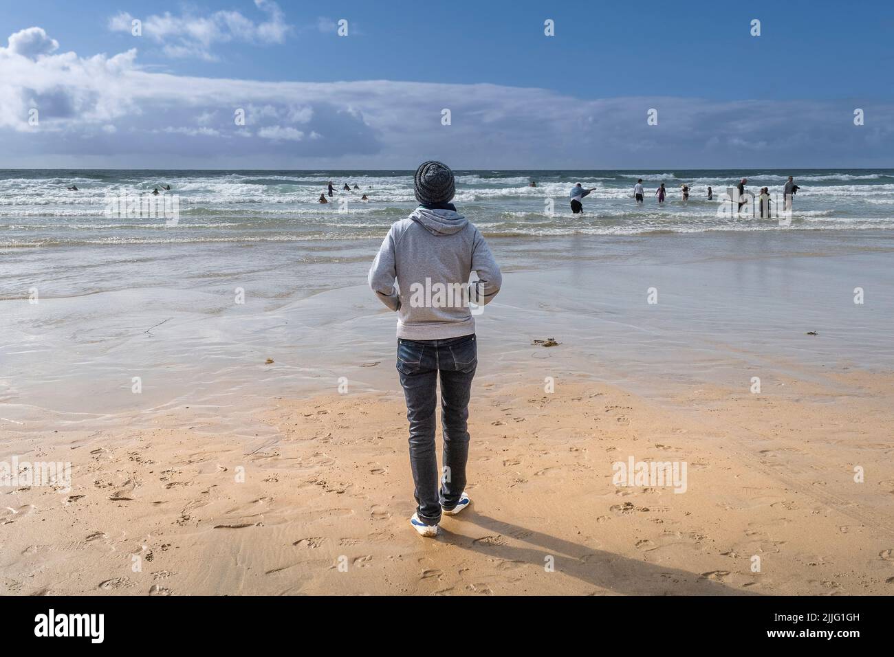 Rear view of a man standing alone on Fistral Beach looking out to sea in Newquay in Cornwall in England in the UK. Stock Photo