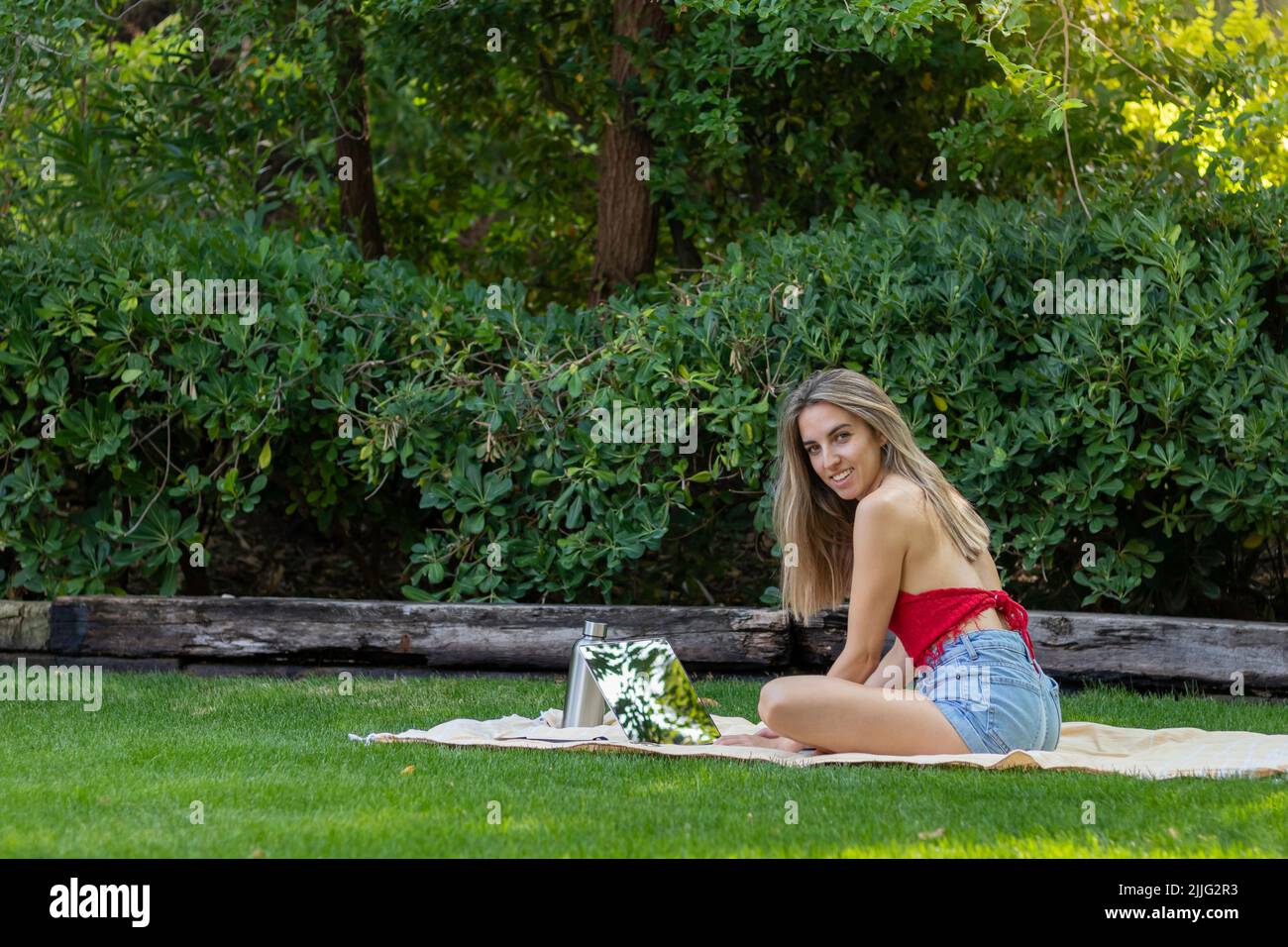 Young blonde woman looking to camera and smiling having a good time using her tablet in the city park Stock Photo