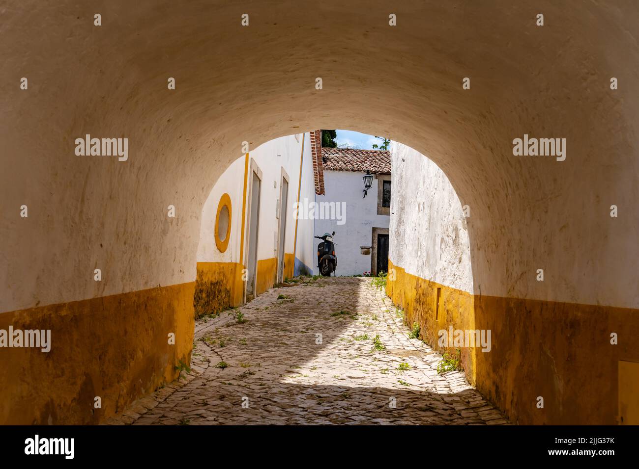 View of a cobbled backyard with access through the thick ramparts of the fortress in Obidos, Portugal Stock Photo