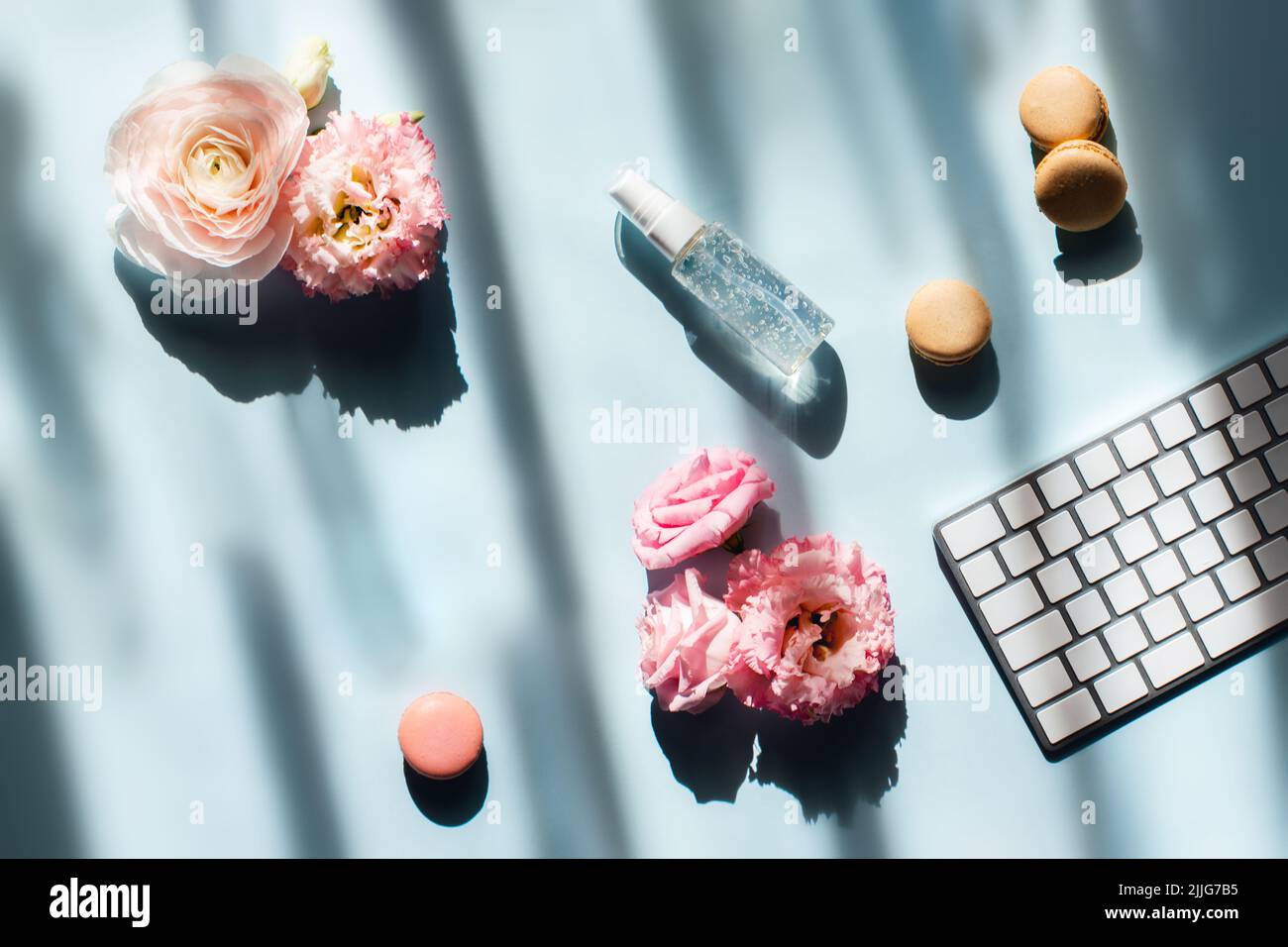 Workspace in sunlight. Computer keyboard, next to window, hand cream or sanitizer, cakes and flowers. Stock Photo