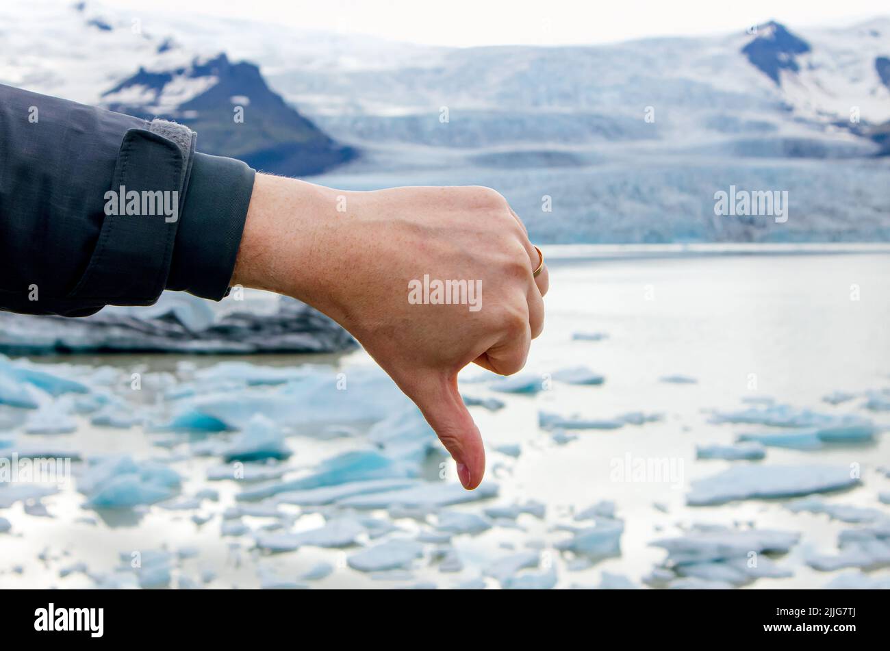Person hand showing thumb down emotion towards climate change and global worming. Melting glacier on background. Stock Photo