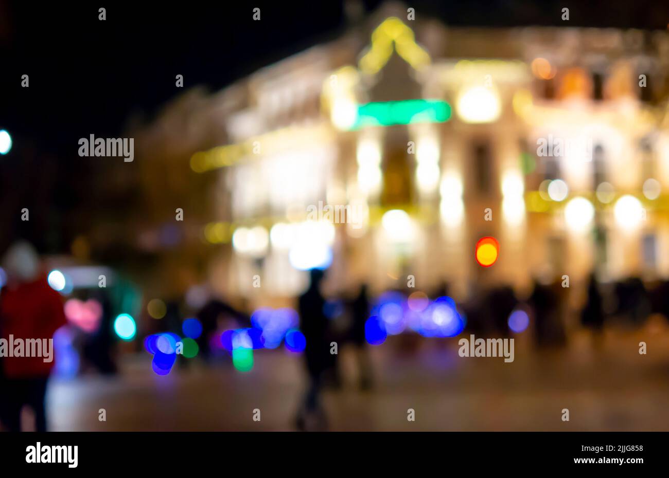 Blurred background. Blurred black silhouettes of people, blurred silhouette of architectural building illuminated by lanterns, backlight at night. City square in evening. Lots of people on city street Stock Photo