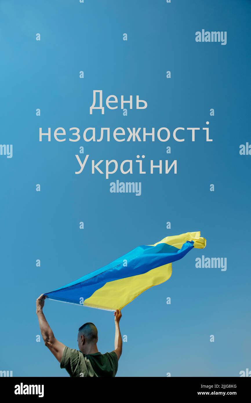 the text independence day of ukraine written in ukrainian and a man waving the ukrainian flag on the sky above his head, in a sunny day Stock Photo