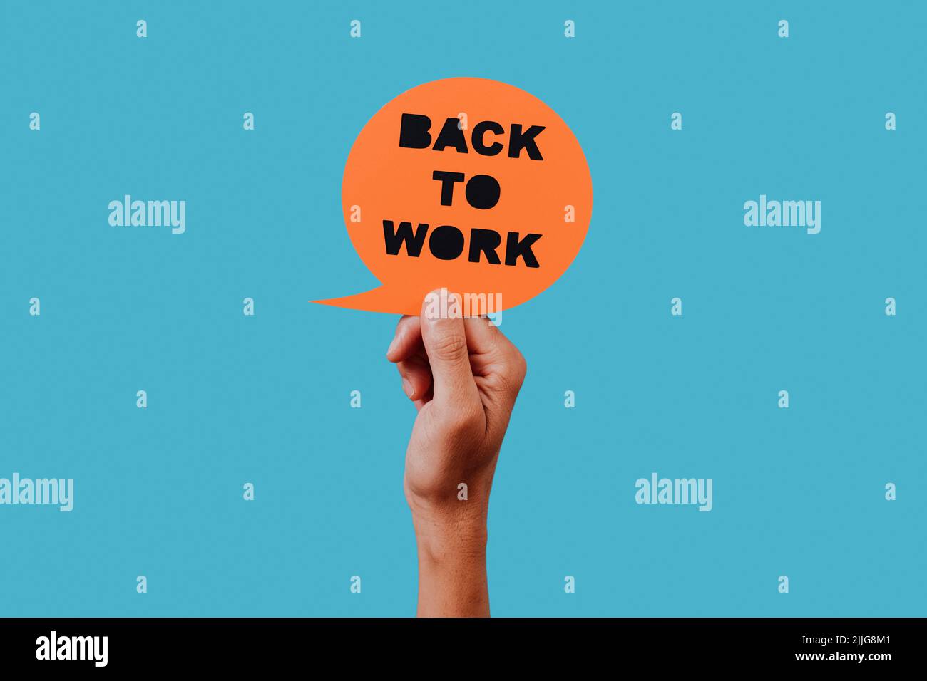man holds an orange paper sign, in the shape of a speech bubble, with the text back to work in it, on a blue background Stock Photo