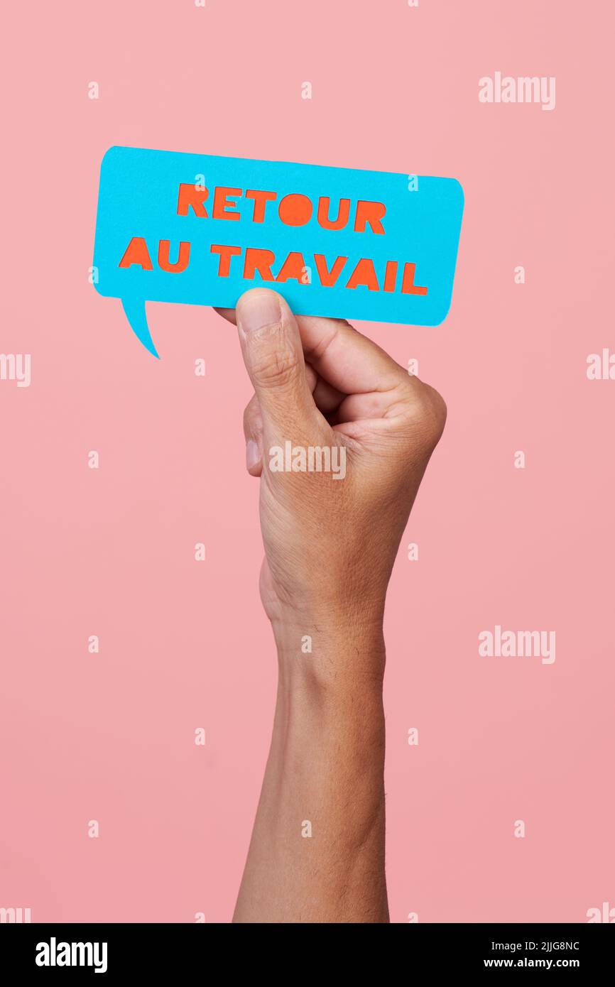 closeup of a man holding a blue paper speech bubble with the text back to work written in french, on a pink background Stock Photo