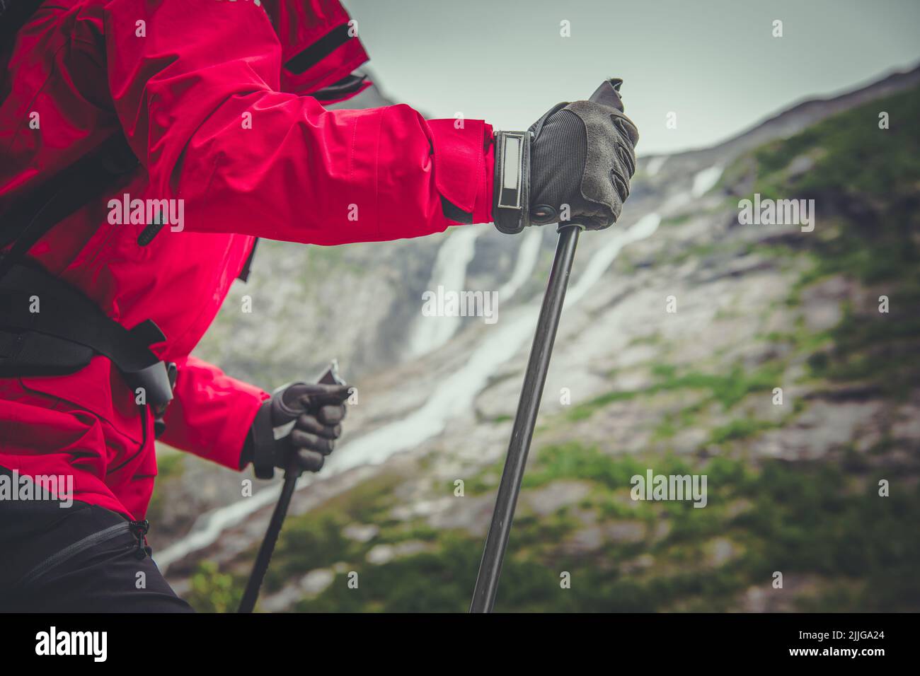 A Person in Red Winter Jacket and Protective Gloves Hiking With Poles and Backpack Among the Scenic Mountain Views. Outdoor Activities Theme. Stock Photo