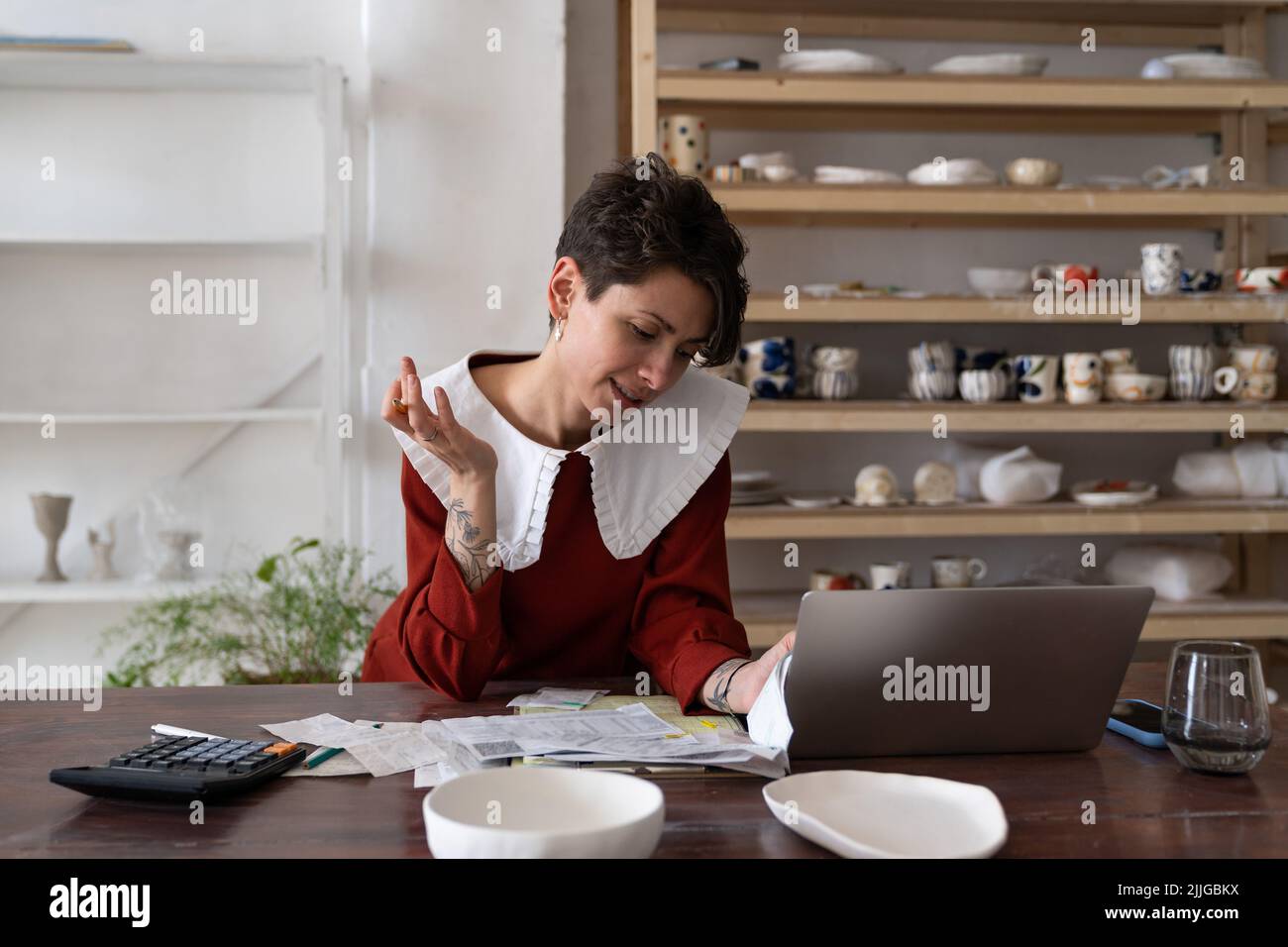Focused young woman ceramic studio owner analyzing bills and receipts
