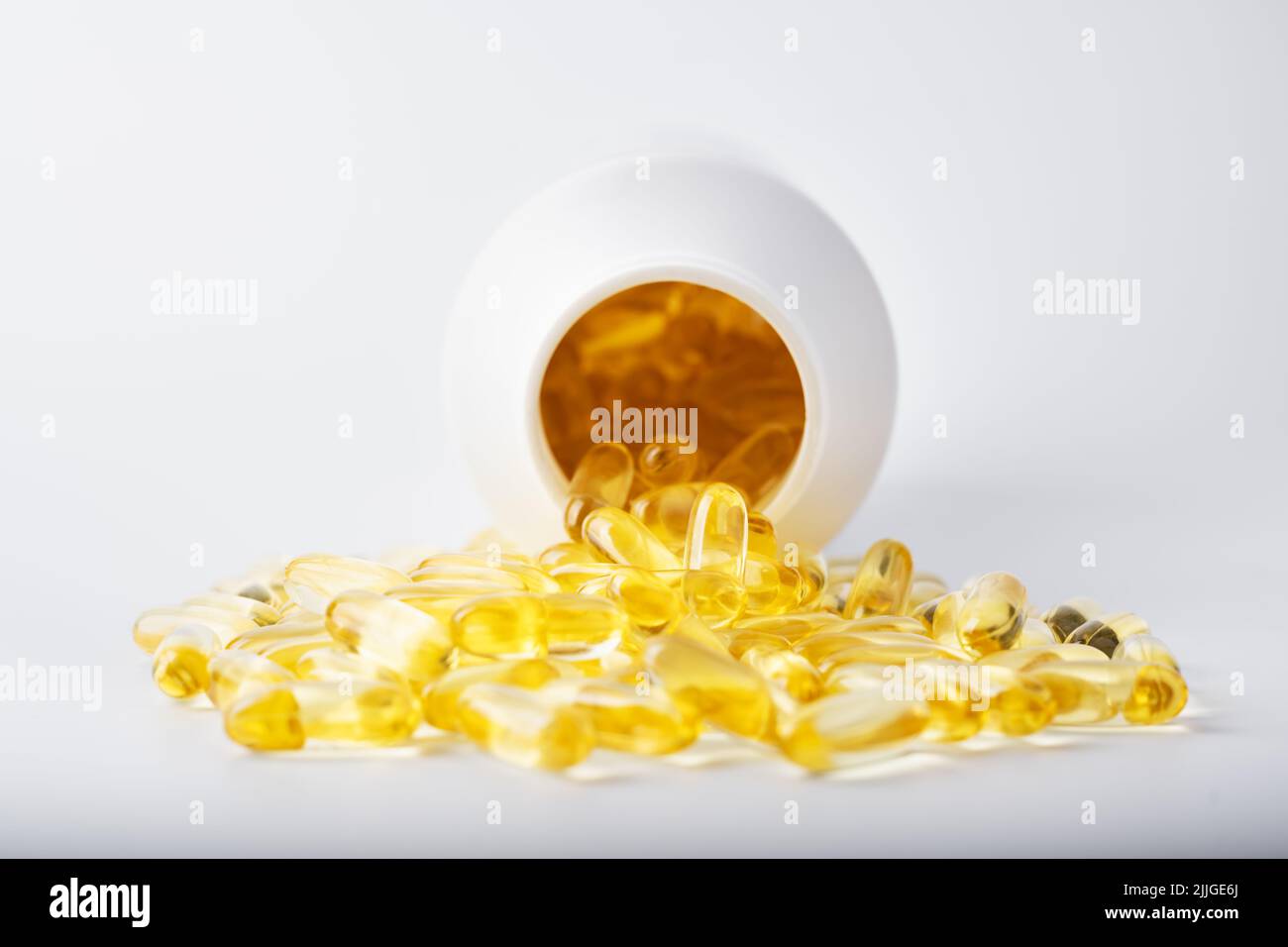 Yellow fish oil capsules in a jelly shell near the white jar. Vitamins and dietary pills supplements. Health concept Stock Photo