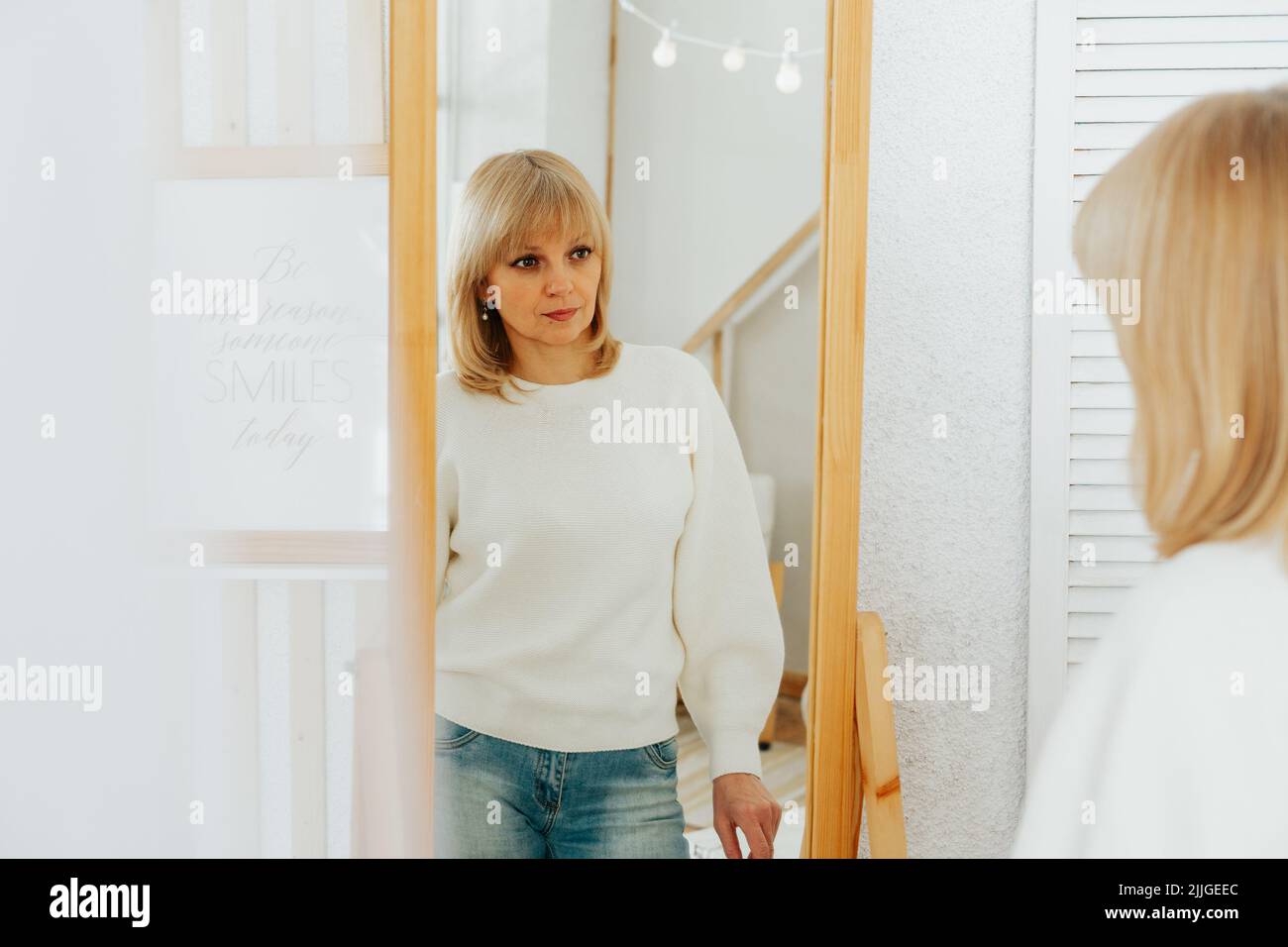 woman standing near mirror and looking at reflection Stock Photo