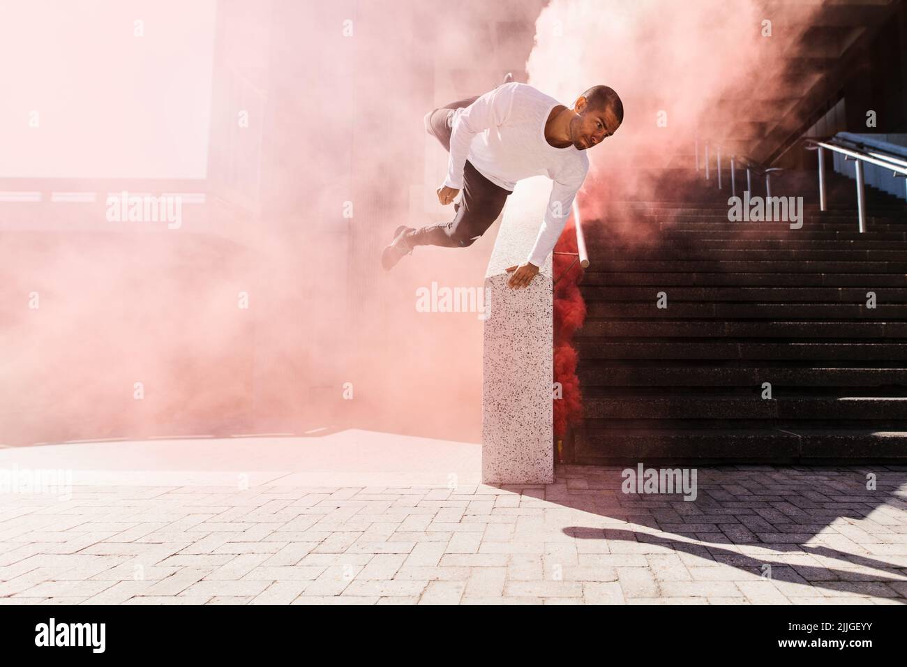 Young man practicing parkour and free running with a smoke grenade. Young male athlete practicing parkour in an urban space. Stock Photo