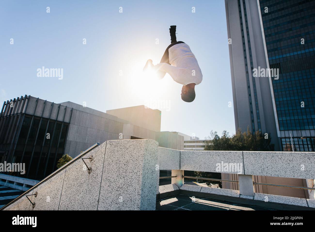 Athletic man practicing parkour and free running by doing a frontflip from a obstacle outdoors. Sporty young man practicing extreme sport activities o Stock Photo