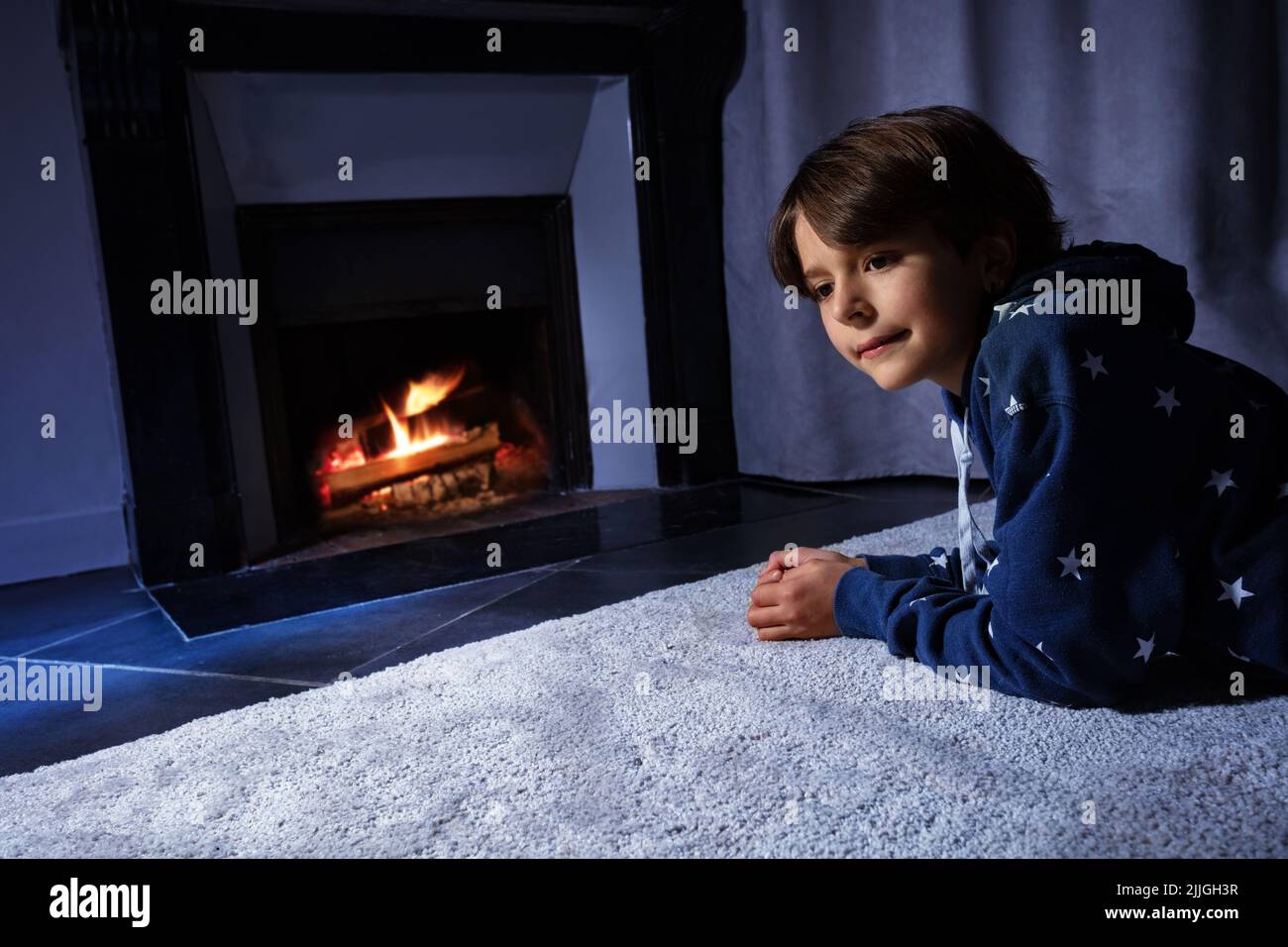 Boy lay in front of the home fireplace look at fire Stock Photo