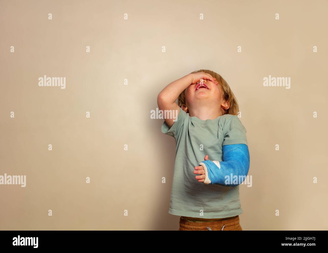 Crying boy with broken hand stand over wall Stock Photo