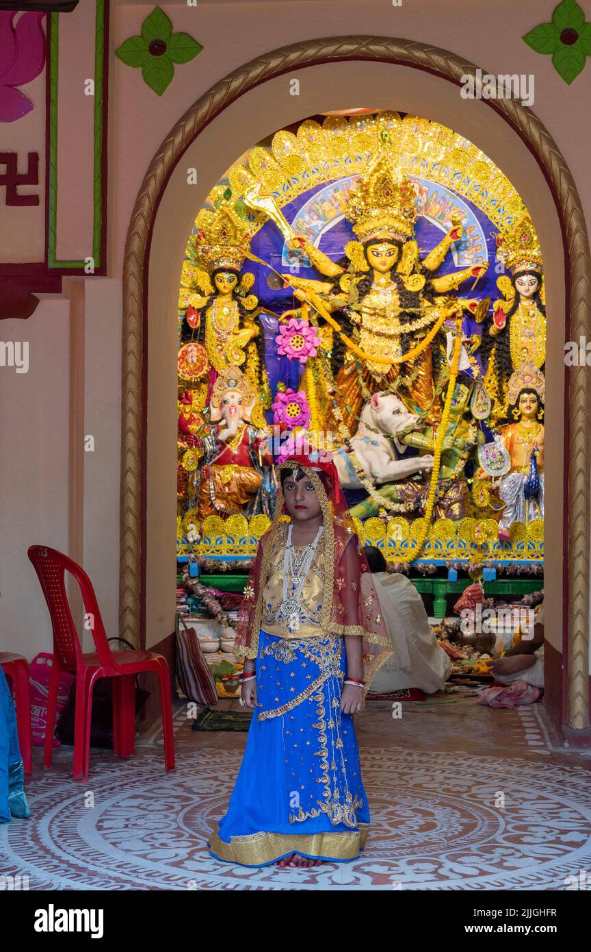 Howrah,India -October 26th,2020 : Bengali girl child posing with Goddess Durga in background, inside old age decorated home. Durga Puja festival. Stock Photo