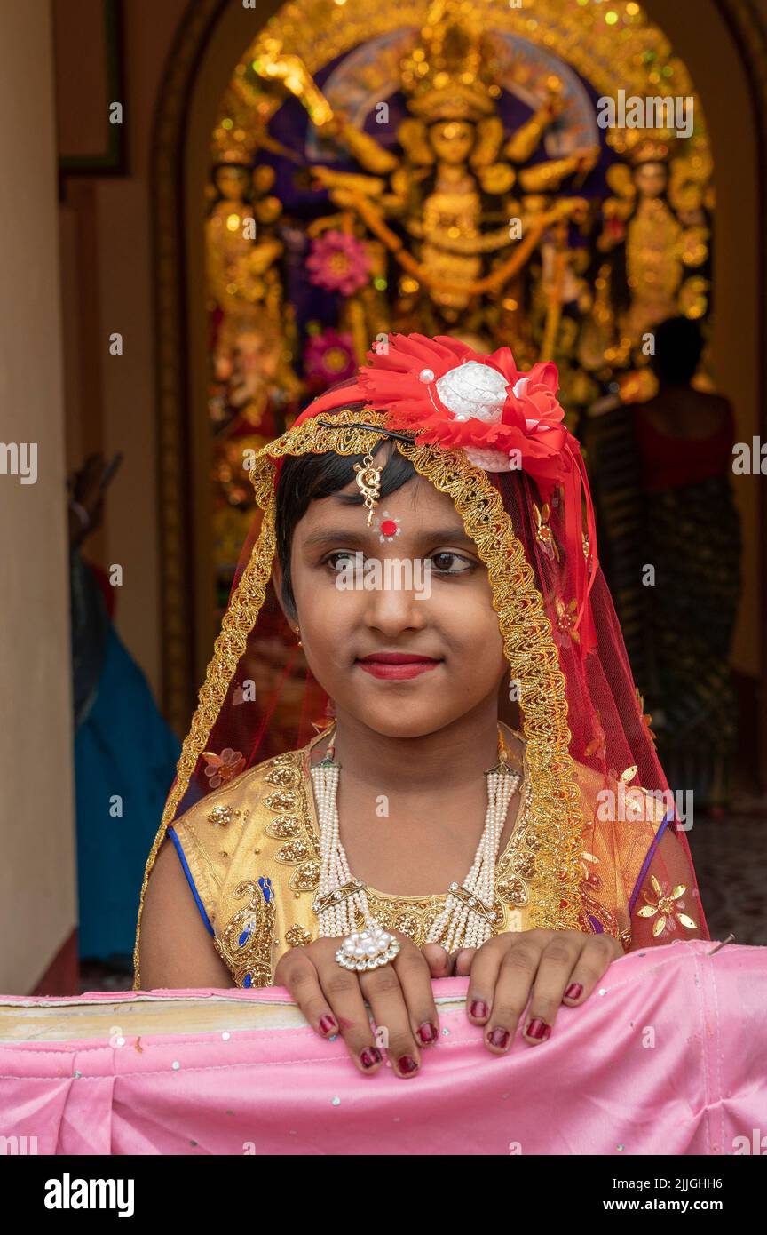Howrah,India -October 26th,2020 : Bengali girl child in festive dress, smiling and posing with Goddess Durga in background, inside old age home. Stock Photo