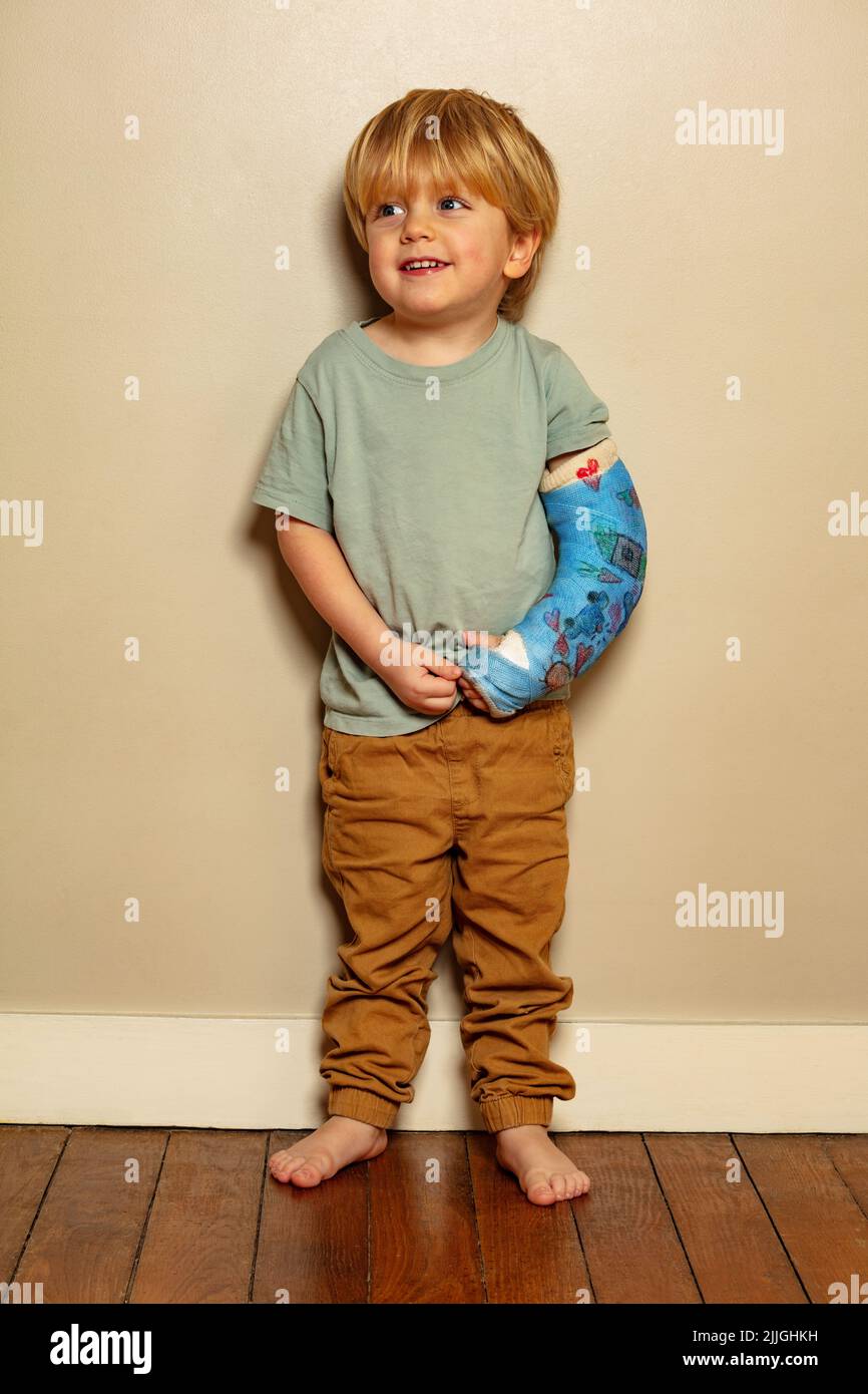 Full height portrait of a boy having positive expression despite broken hand in plaster with drawings cast after accident Stock Photo