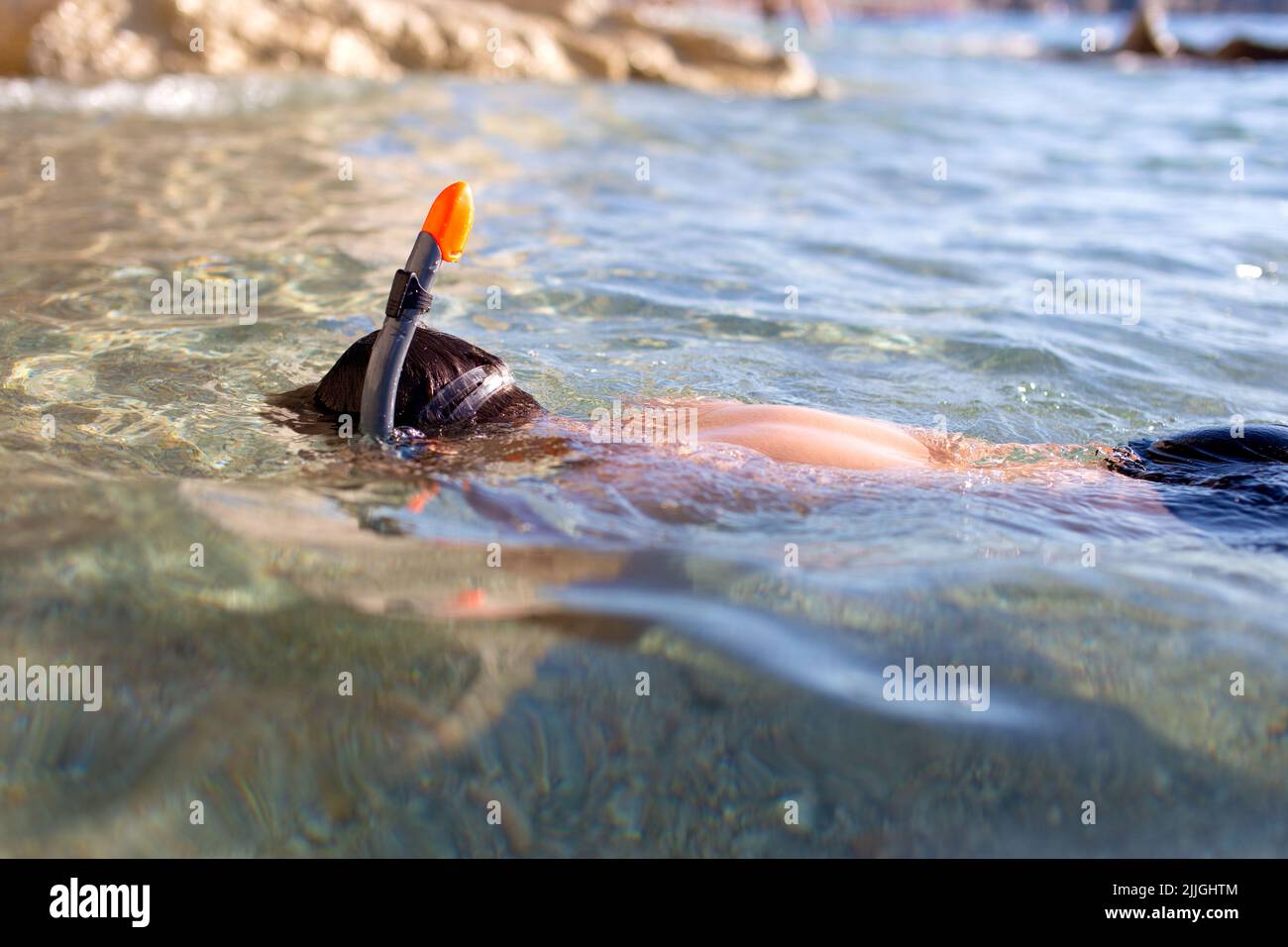 Boy in goggles and pipe diving in sea at rocky shore Stock Photo