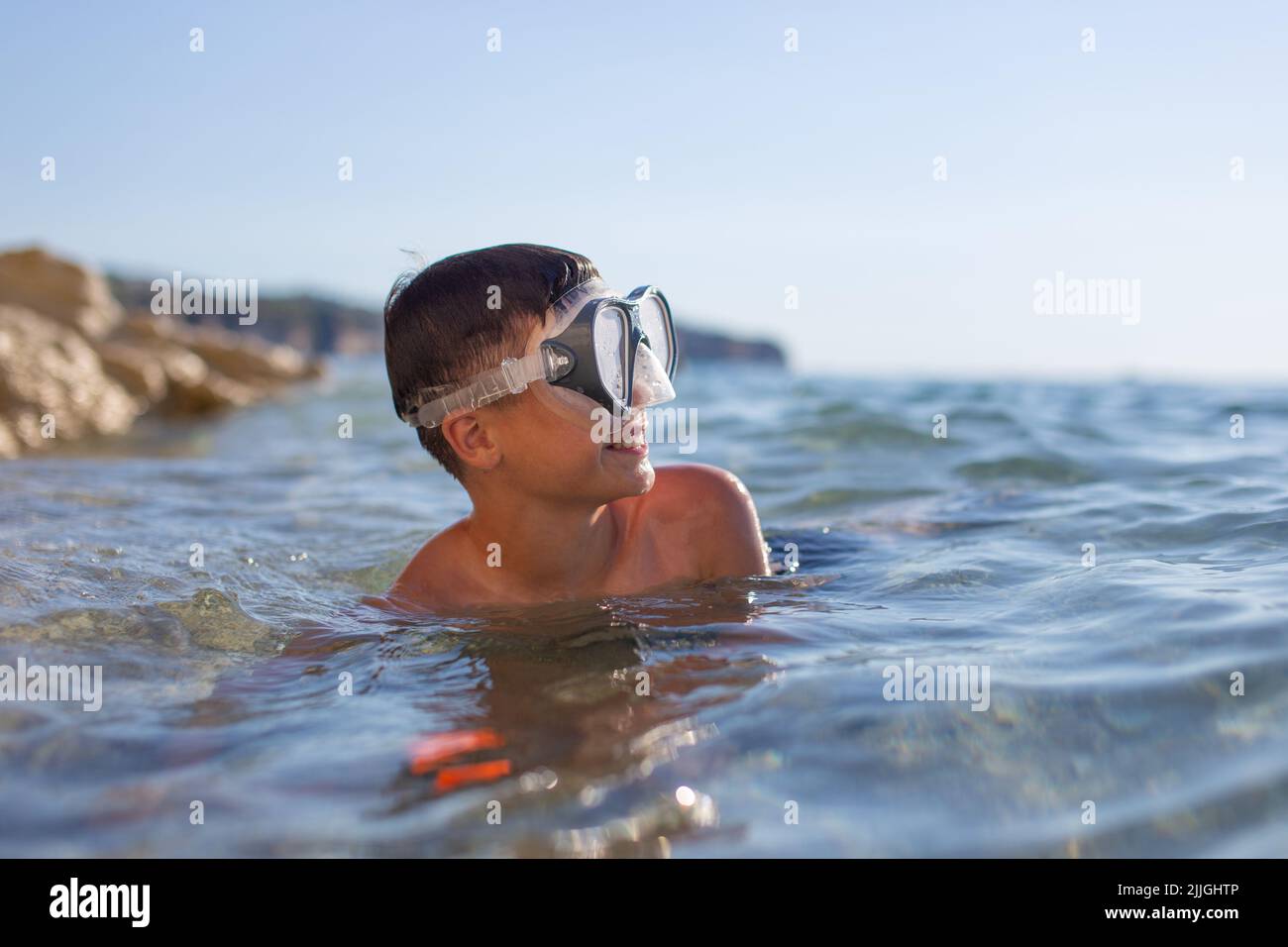 Happy young boy in goggles looking away in sea Stock Photo