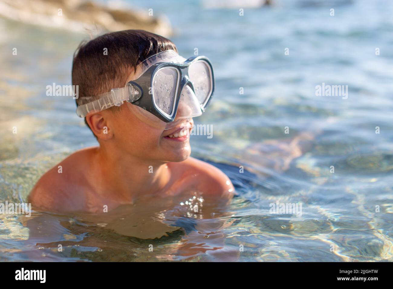 Happy little boy in goggles looking away in sea Stock Photo