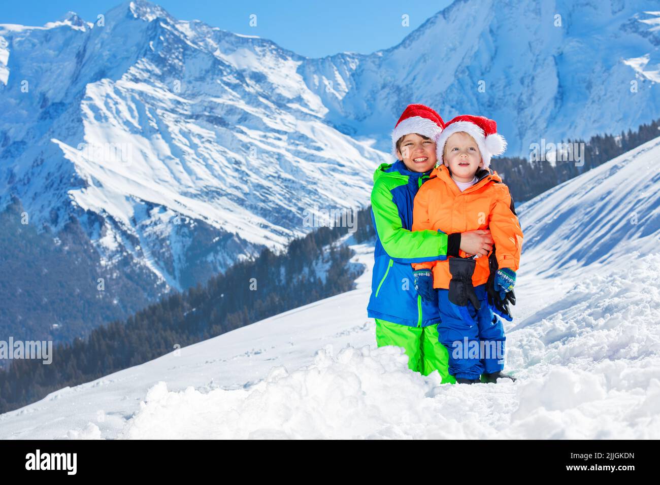 Two boys with Santa hats hug standing over mountains on back Stock Photo