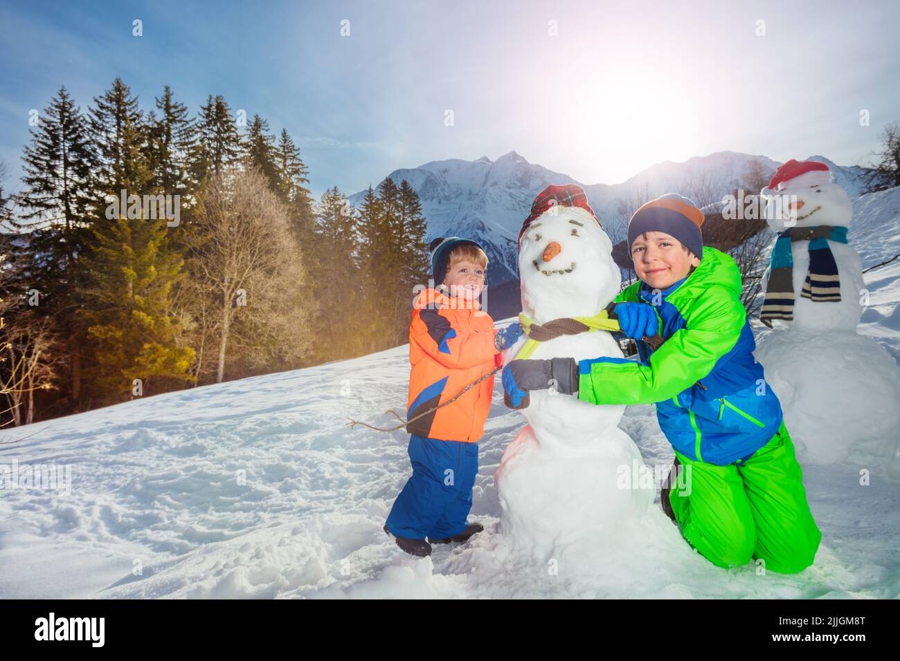 Boys build and dress snowman outside over mountains Stock Photo