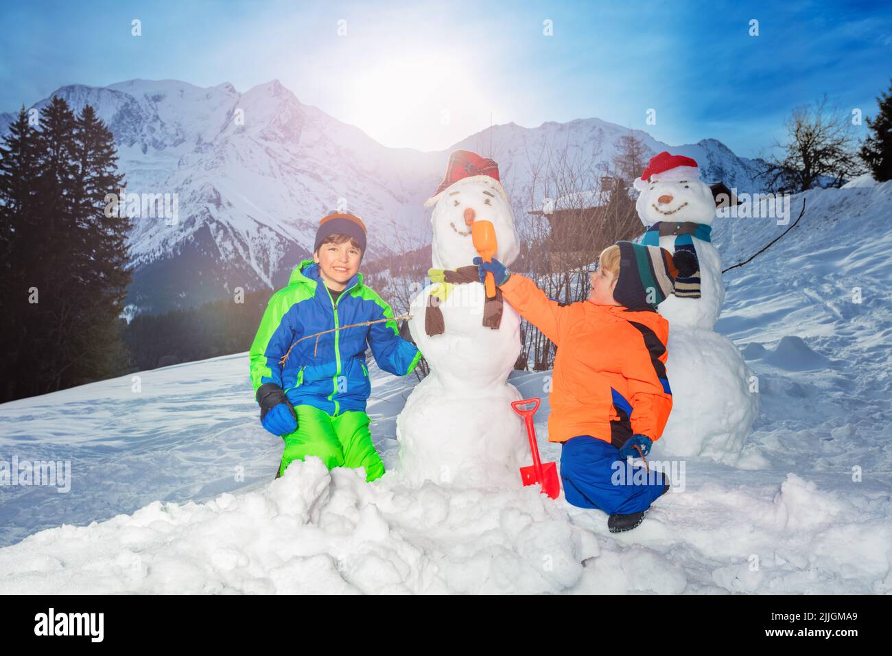 Two brothers, boys build, dress snowman with scarf and hat Stock Photo