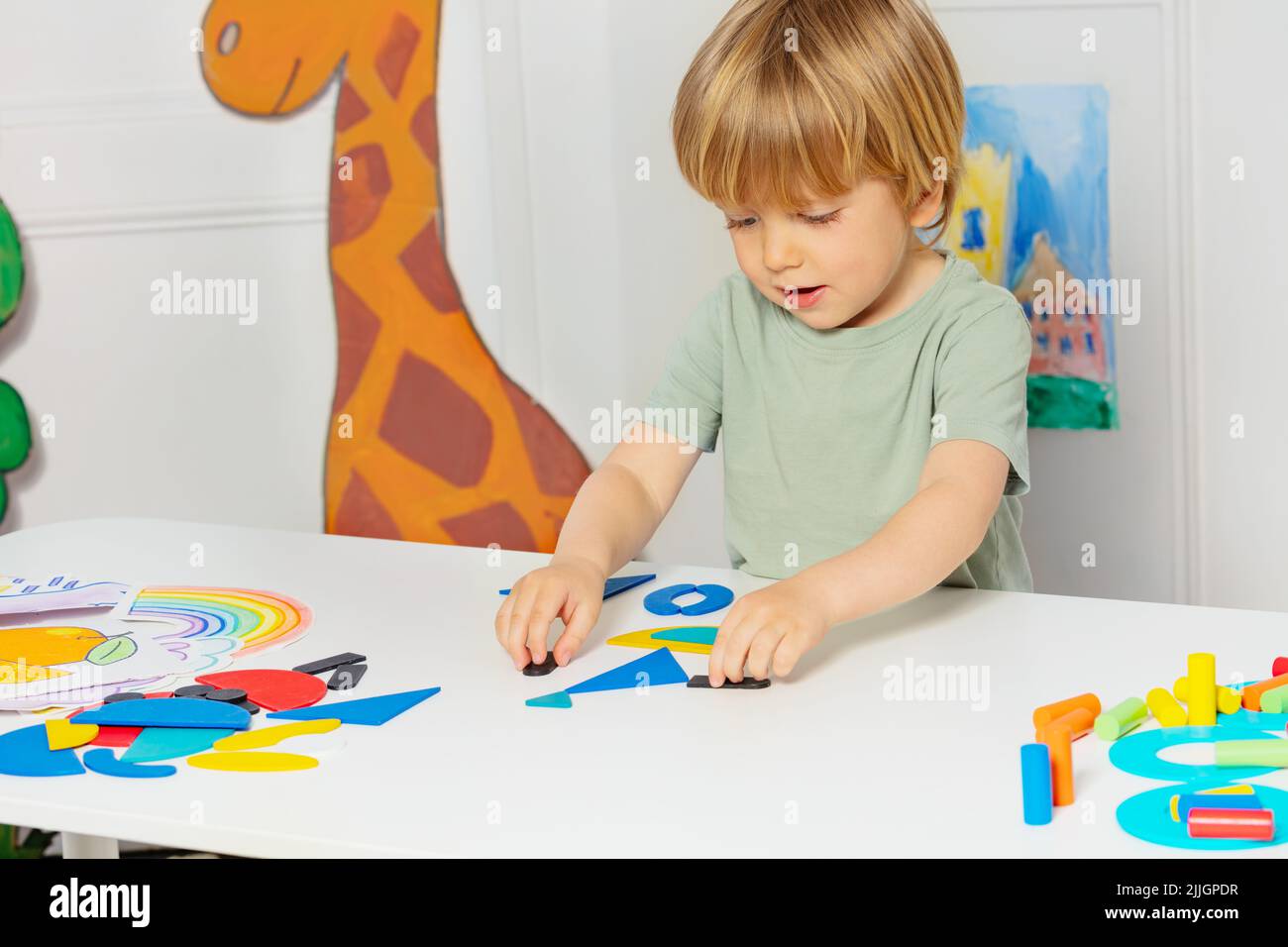 Blond boy form shapes standing by the table in kindergarten Stock Photo