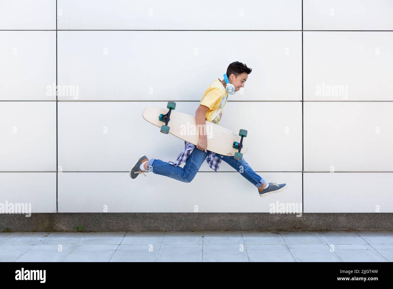 Caucasian teenage boy with longboard jumping. He is isolated on a wall. Urban lifestyle. Space for text. Stock Photo