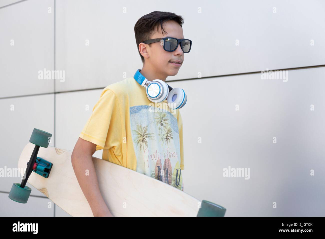 Closeup of caucasian teenage boy with skateboard. He is isolated on a wall. Vacation and urban lifestyle concept. Stock Photo
