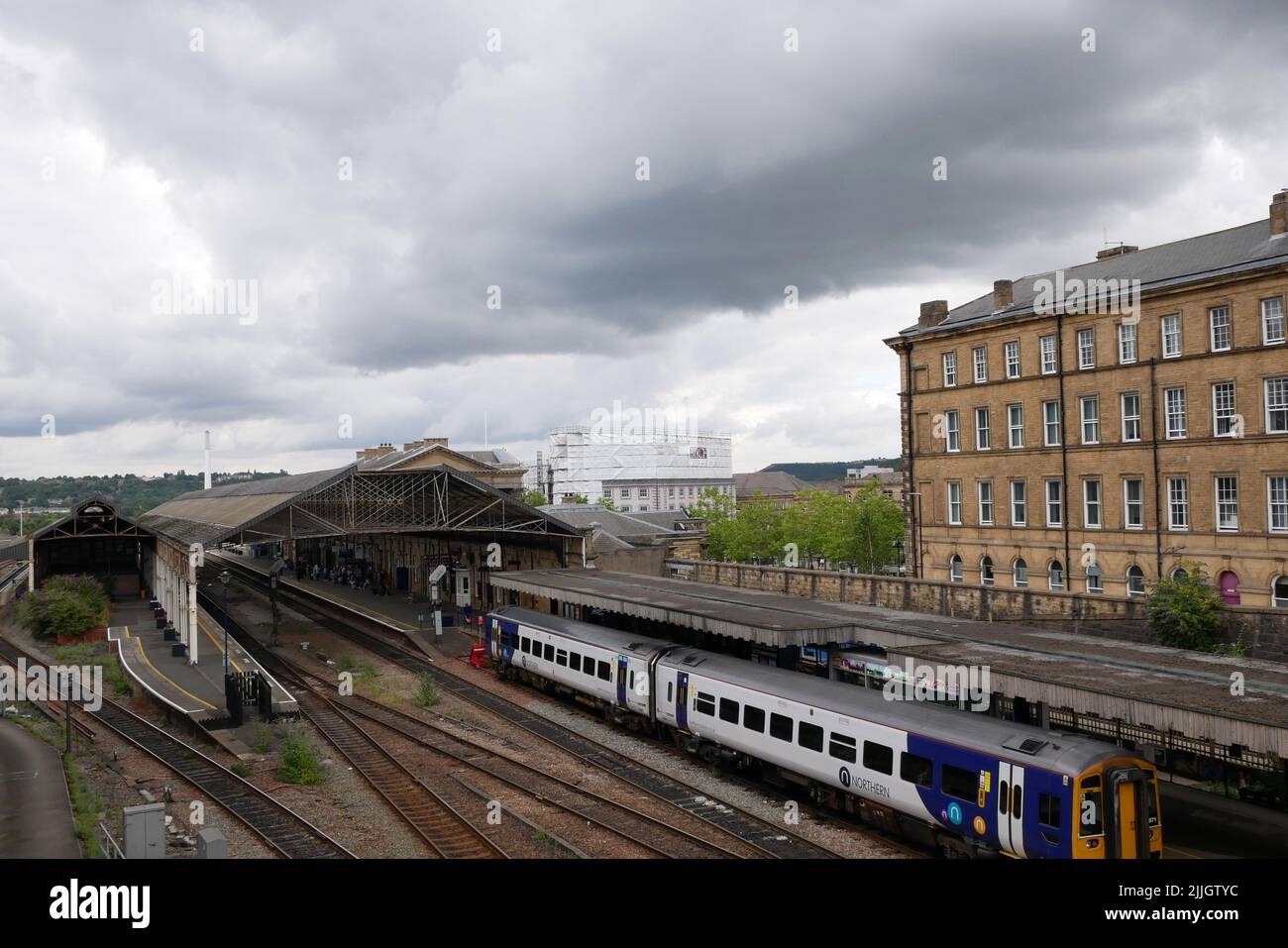 Silver and blue two carriage northern railway train parked in station other lines and buildings cloudy sky Stock Photo