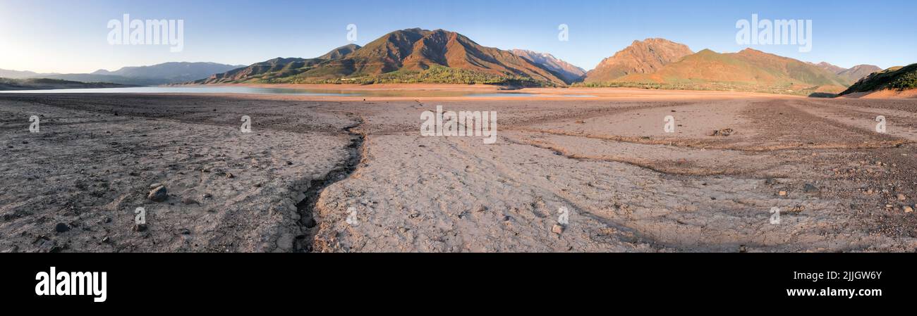 Panorama beautiful landscape with setting sun: mountains, lake and cracked earth - dried-up riverbend. Copy space. Stock Photo