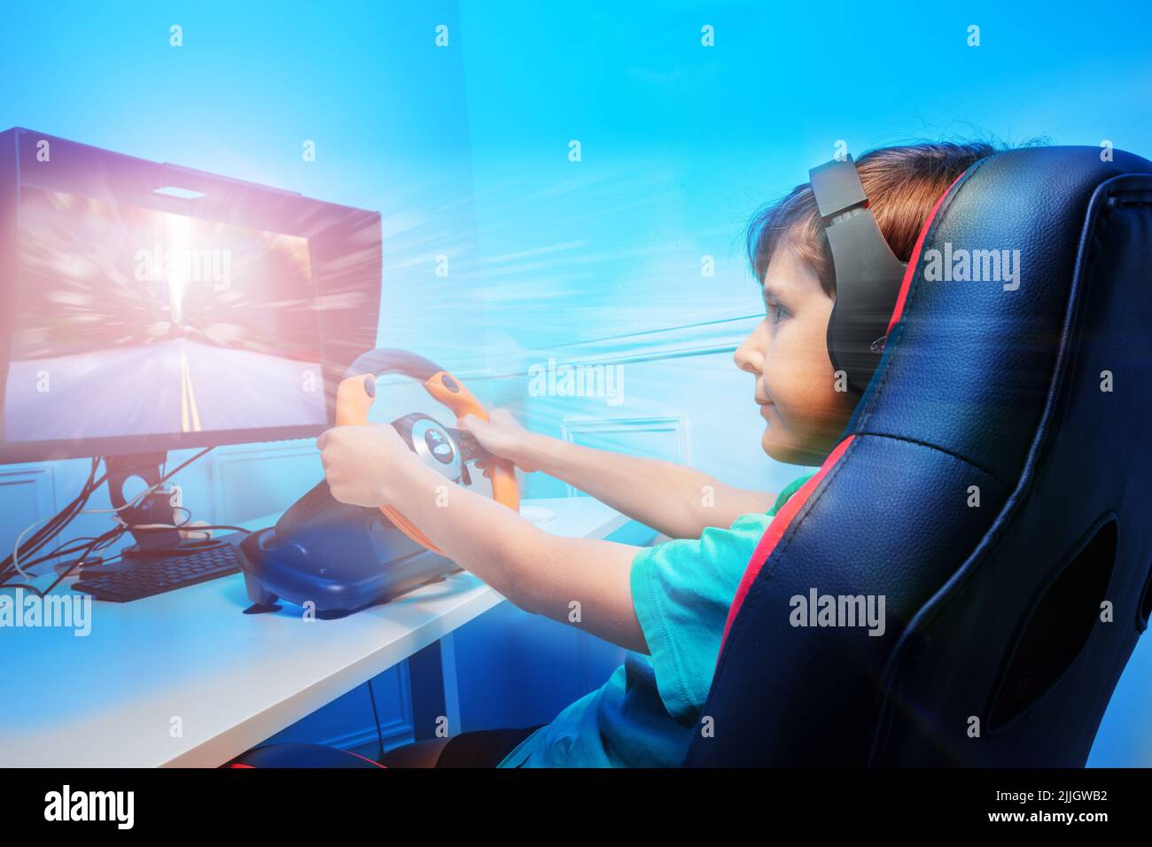 Boy with hands on steering wheel in headphones playing race game Stock Photo