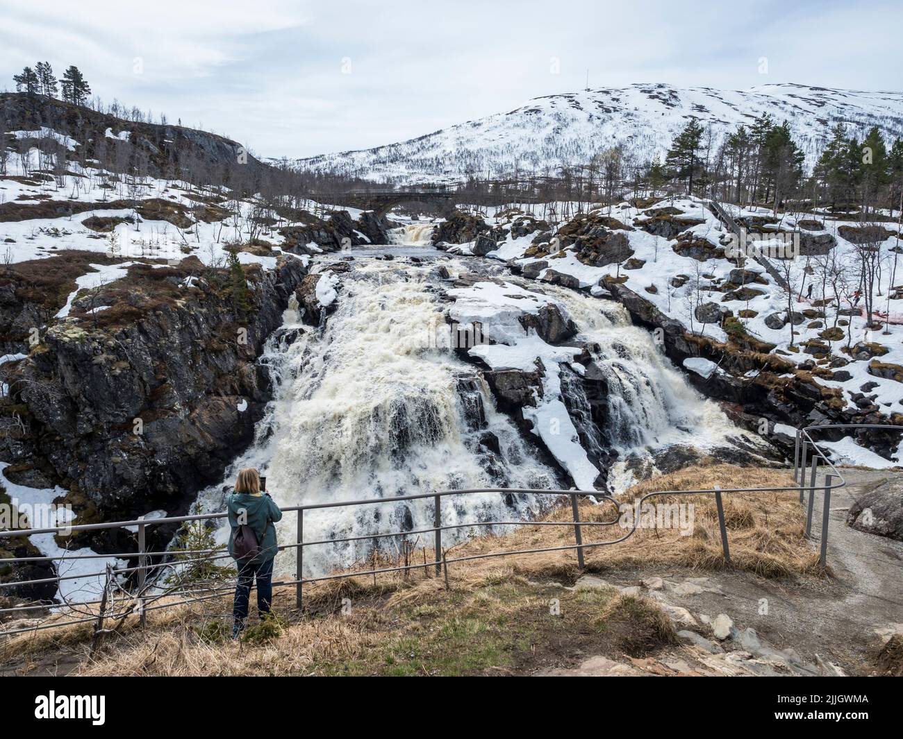 Woman takes pictures at waterfall Voringfoss, snowy in spring, Hardangervidda, Norway Stock Photo