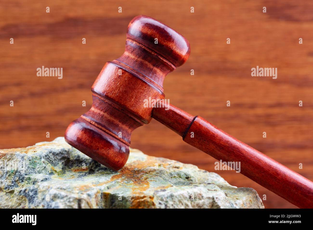 Difficult court and judicial decisions symbolized by gavel placed on rock surface with wood grain background Stock Photo