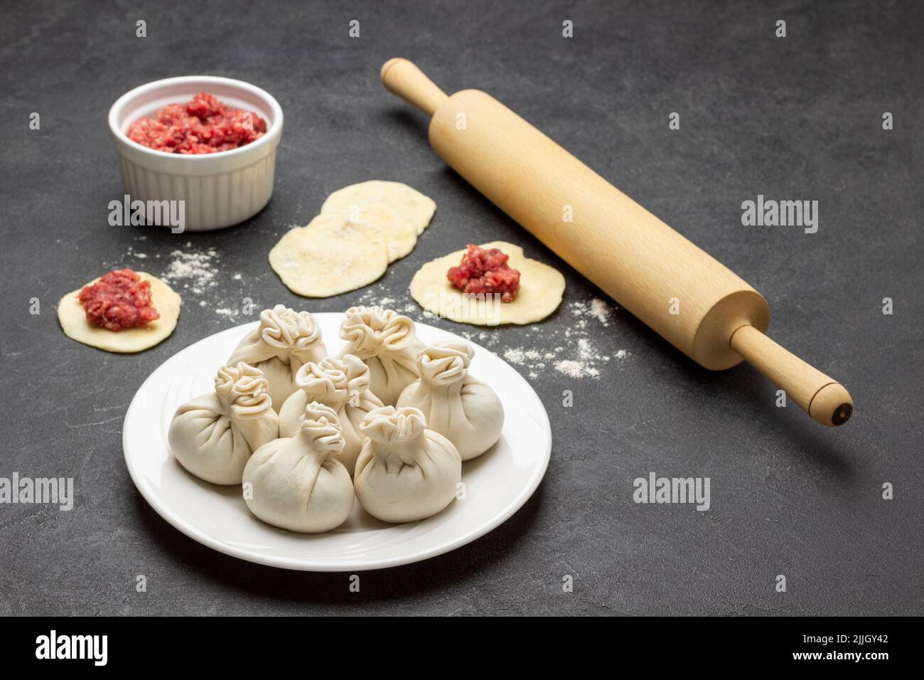 Raw dumplings on plate. Rolling pin and meat filling in bowl. Top view