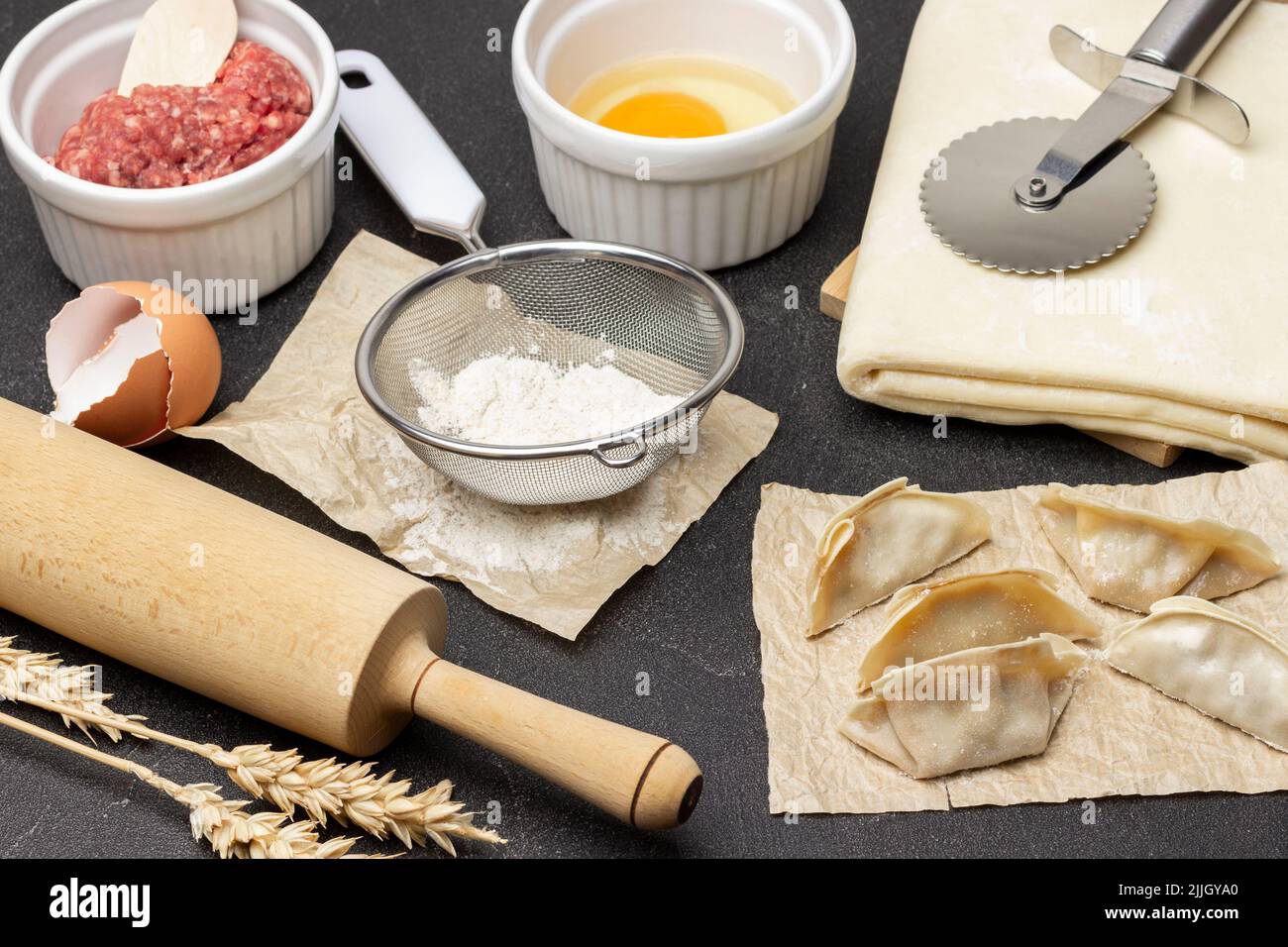 Rolling pin, flour sieve, raw gyoza dumplings on table. Dough, meat filling and egg in bowl. Top
