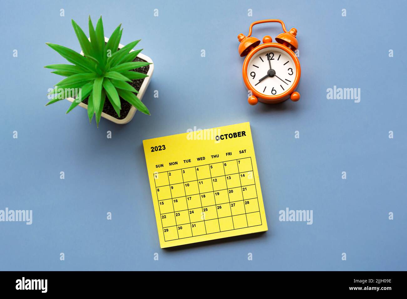 October 2023 calendar on adhesive note with alarm clock set at 8 o