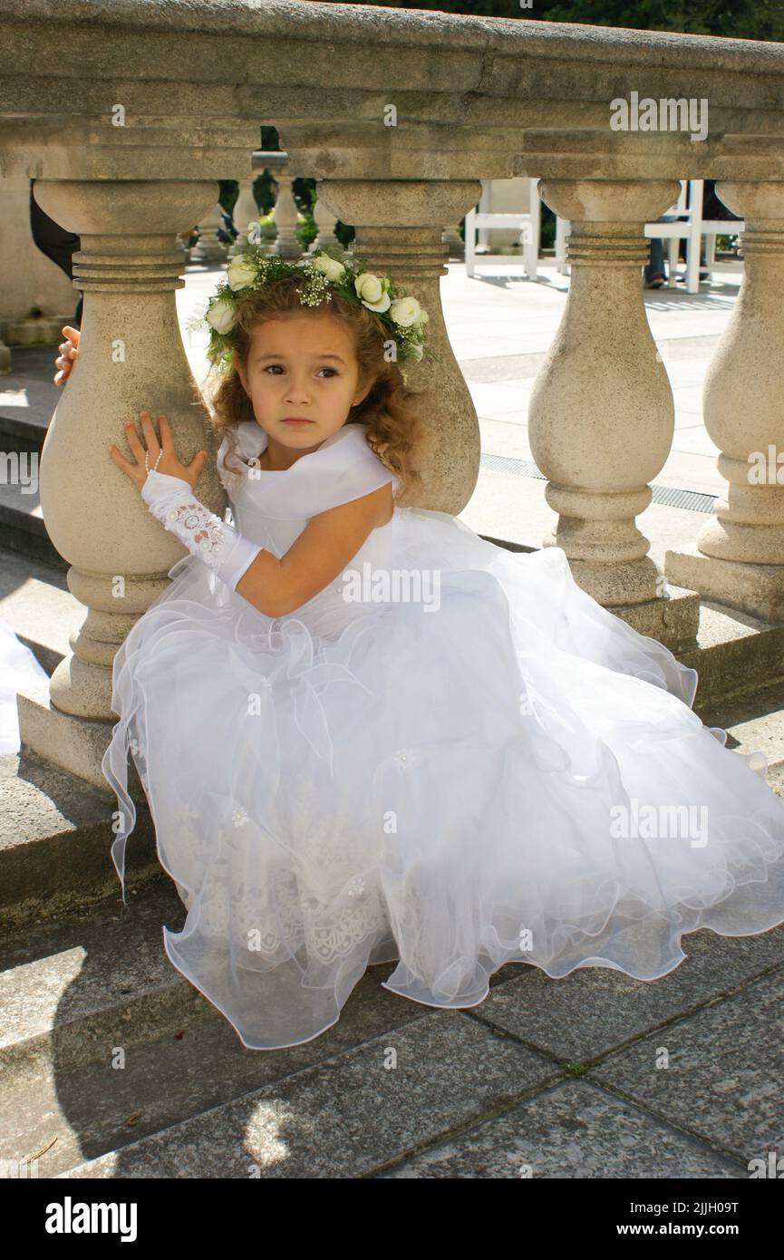 Little beautiful girl in a white elegant dress with a wreath of roses ...