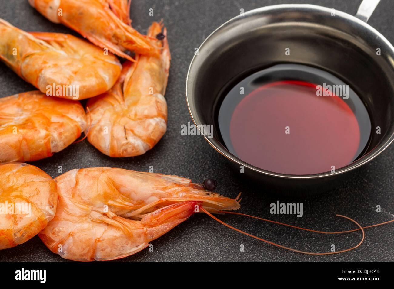 Boiled shrimp and soy sauce in metal bowl. Top view. Black background