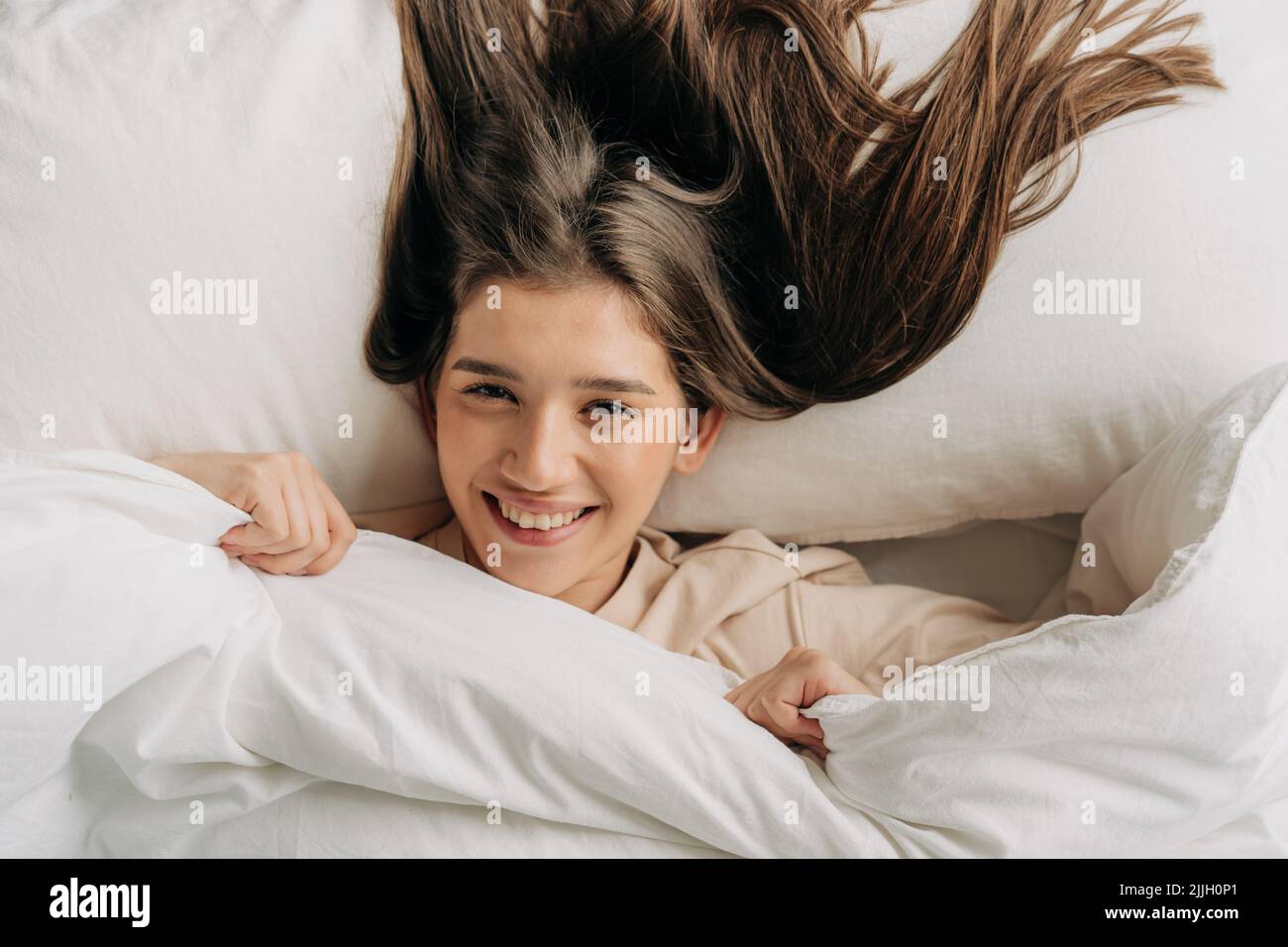 Young smiling lying on the bed under the blanket smiles