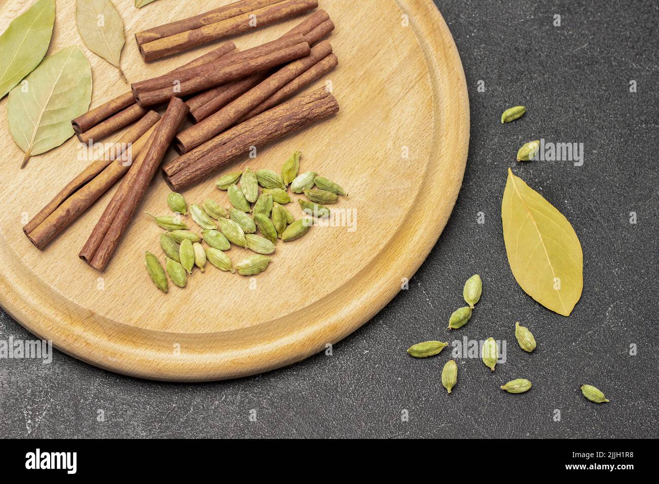 Cardamom, bay leaf and cinnamon sticks on board. Flat lay. Black