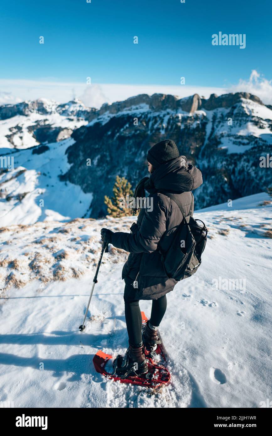 A vertical shot of a girl on skis looking at the snow capped mountains in front in Switzerland Stock Photo