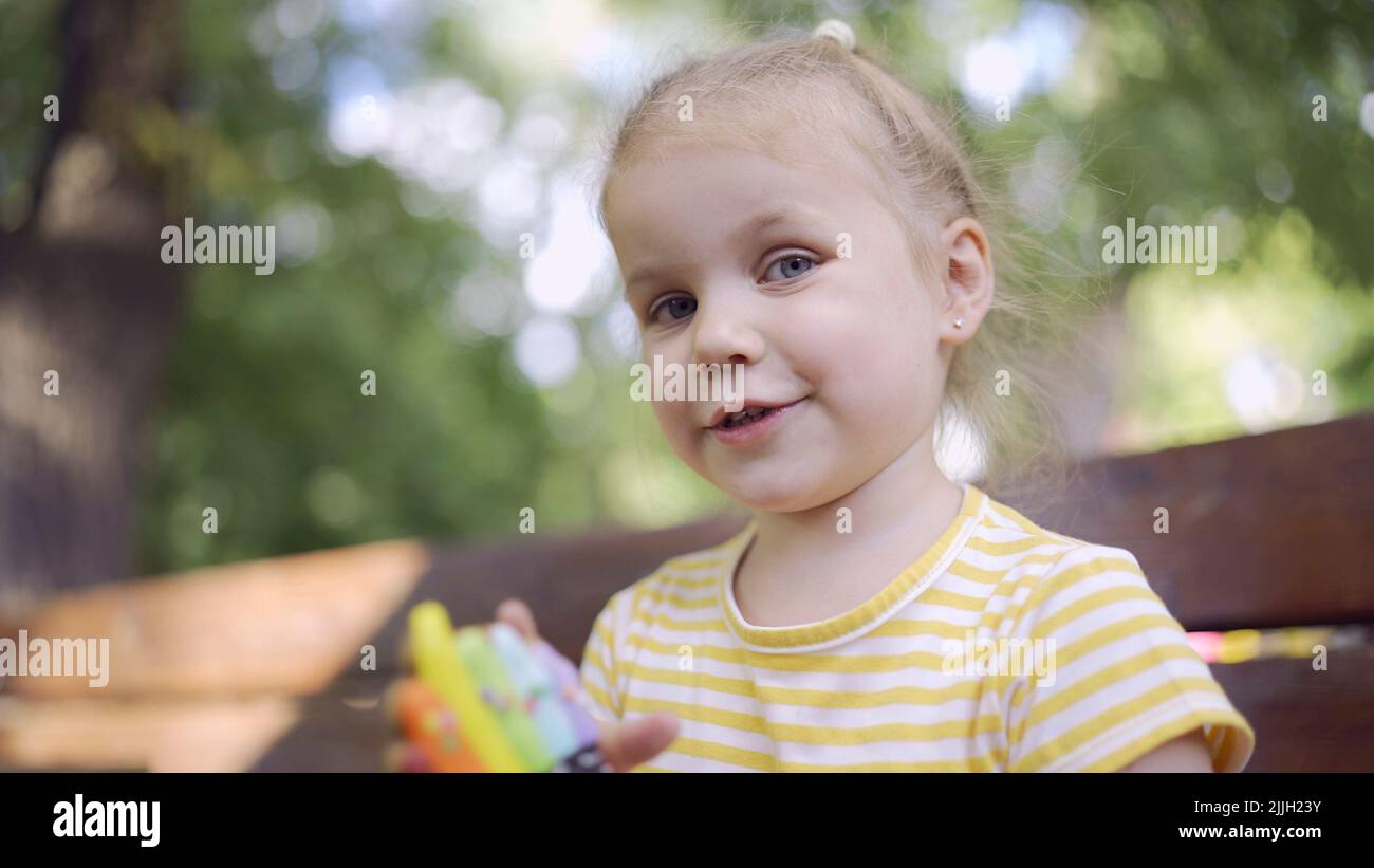 Little girl holds a multi-colored gingerbread and smiles. Close-up portrait of cute child girl sitting on park bench with cookies in looks into the ca Stock Photo