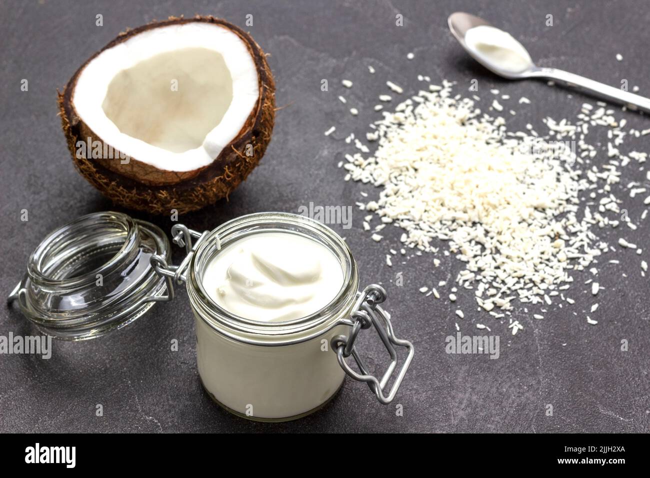Half coconut and glass jar of coconut yogurt. Coconut flakes on table
